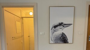 Un corridoio con pavimento in legno, una porta illuminata e un quadro con soggetti naturalistici appeso al muro.