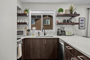 Una cocina moderna con armarios de madera oscura, una encimera blanca, horno empotrado, un lavabo y una ventana con persianas.