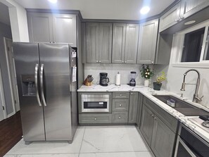 A modern kitchen with grey cabinets, a stainless steel refrigerator, an oven, a sink, and a window.