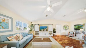 A living room with a sofa, coffee table, TV, and a view of the ocean. - Sombrero Sanctuary ~ Pet Friendly Pool Home, Steps to the Beach! (Marathon)
