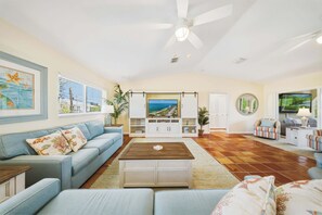 Ein Wohnzimmer mit Sofa, Couchtisch, Fernseher und Blick aufs Meer.