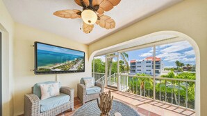 A balcony with wicker furniture, a ceiling fan, and a TV displaying a scenic view. - Sombrero Sanctuary ~ Pet Friendly Pool Home, Steps to the Beach! (Marathon)