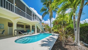 A swimming pool with a covered area, palm trees, and a two-story building with a balcony. - Sombrero Sanctuary ~ Pet Friendly Pool Home, Steps to the Beach! (Marathon)