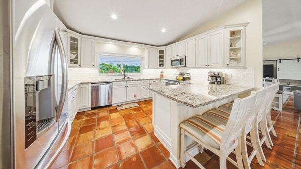 A kitchen with white cabinets, a large island with seating, a dishwasher, and a window with a view. - Sombrero Sanctuary ~ Pet Friendly Pool Home, Steps to the Beach! (Marathon)