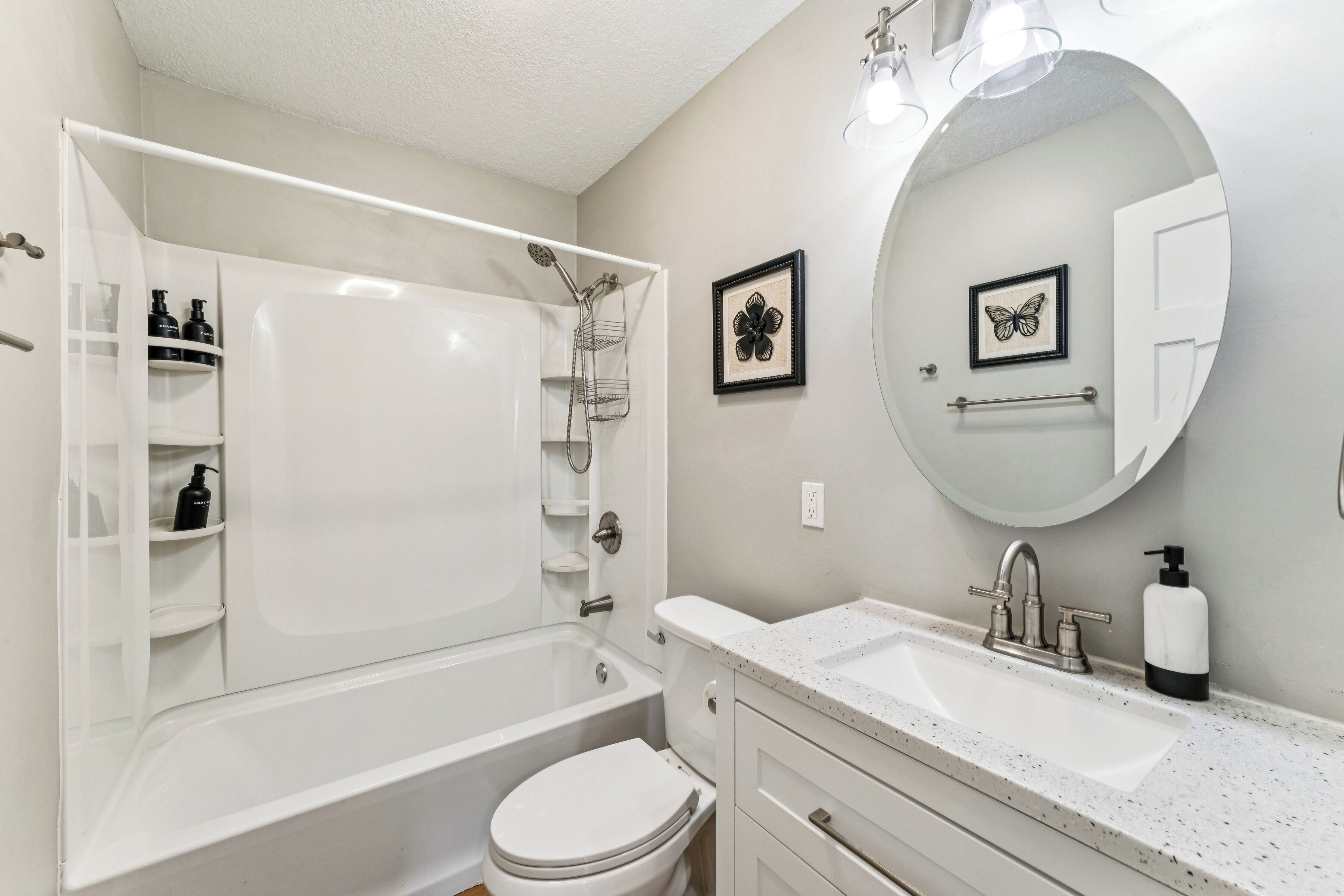 A bathroom with a bathtub, toilet, sink, and a round mirror.
