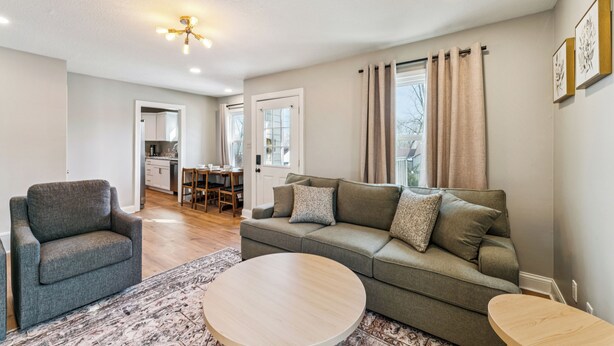 A living room with a sofa, armchair, and coffee table, a kitchen in the background, and a dining area. - Sleeps 6, Quiet & Safe, Easy drive to Arrowhead! (Overland Park)