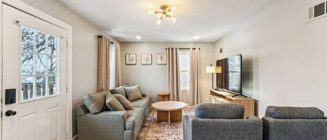 A modern living room with a sofa, armchairs, a coffee table, a TV, and a ceiling light.