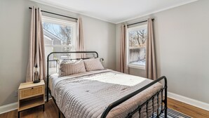 A bedroom with a bed, a bedside table, a lamp, and a window. - Sleeps 6, Quiet & Safe, Easy drive to Arrowhead! (Overland Park)