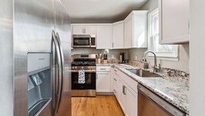 A modern kitchen with stainless steel appliances, white cabinetry, a granite countertop, and a built-in dishwasher. - Sleeps 6, Quiet & Safe, Easy drive to Arrowhead! (Overland Park)