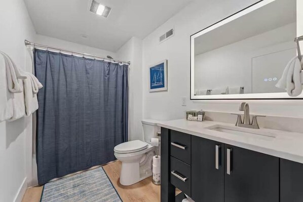 Un bagno moderno con tenda doccia, water, lavabo e specchio.