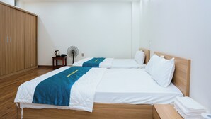 Hotellihuone, jossa on kaksi sänkyä, puinen vaatekaappi, pieni pöytä ja vedenkeitin sekä tuuletin.