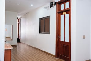 A hallway with wooden flooring, a wooden door with a number plate, and a window with a metal frame. - Vang Anh 2 Hotel Bac Ninh (Bac Ninh)