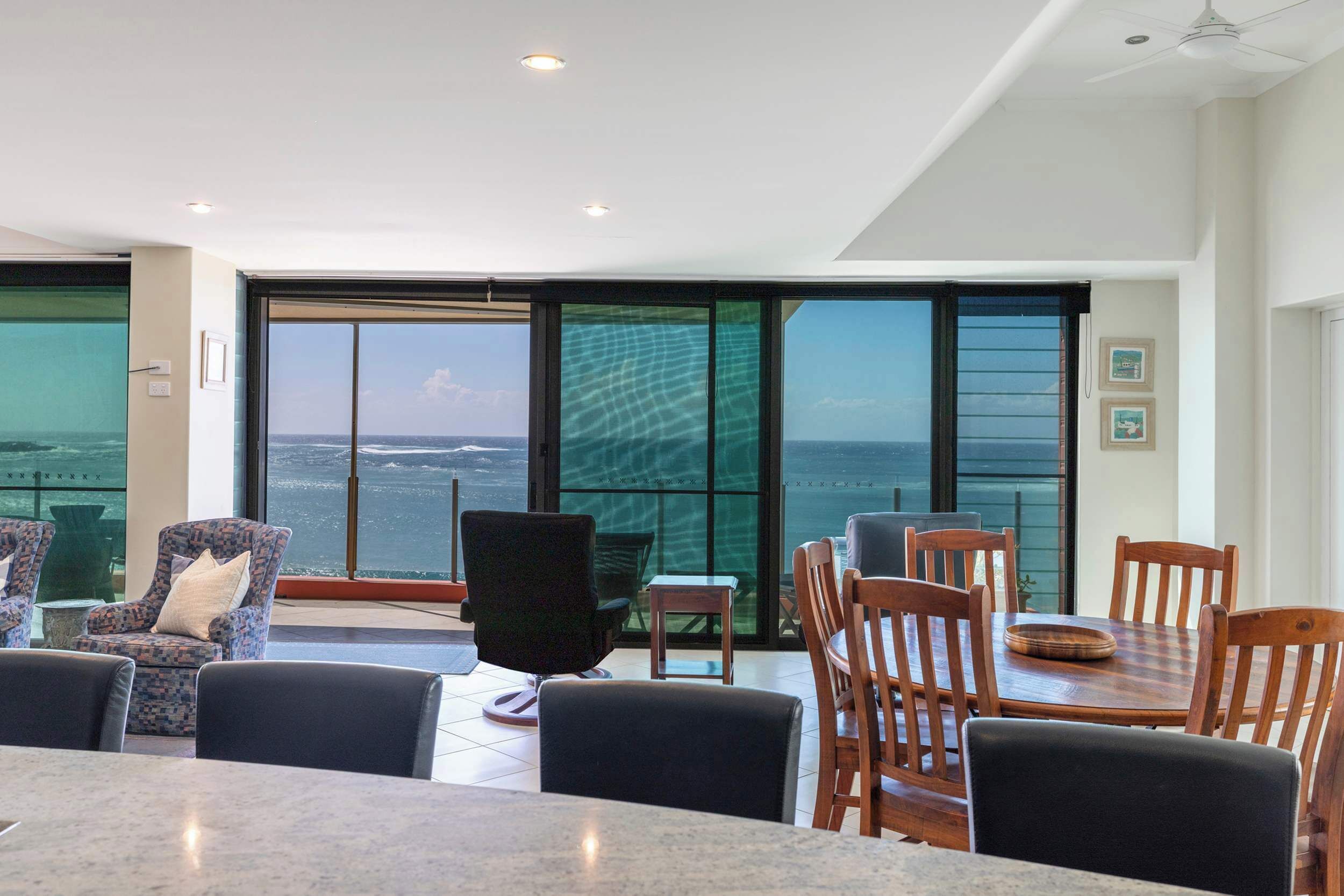 Un comedor moderno con vista al océano, amplias ventanas y una mezcla de muebles modernos y clásicos.
