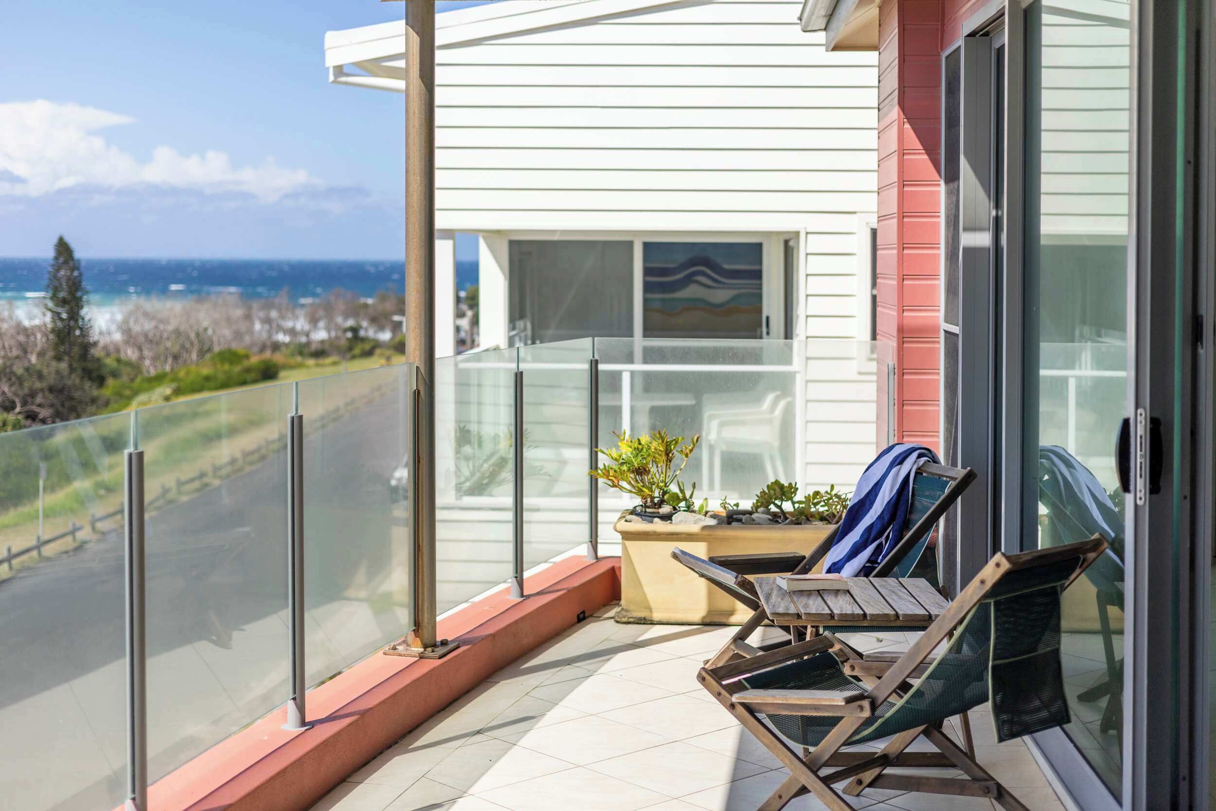 A balcony with a view of the ocean, a potted plant, and a wooden chair.