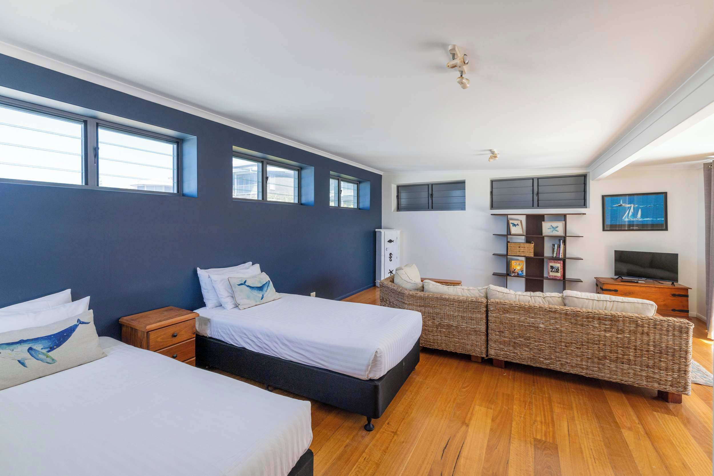 A bedroom with two beds, a sofa, a TV, and a bookshelf.