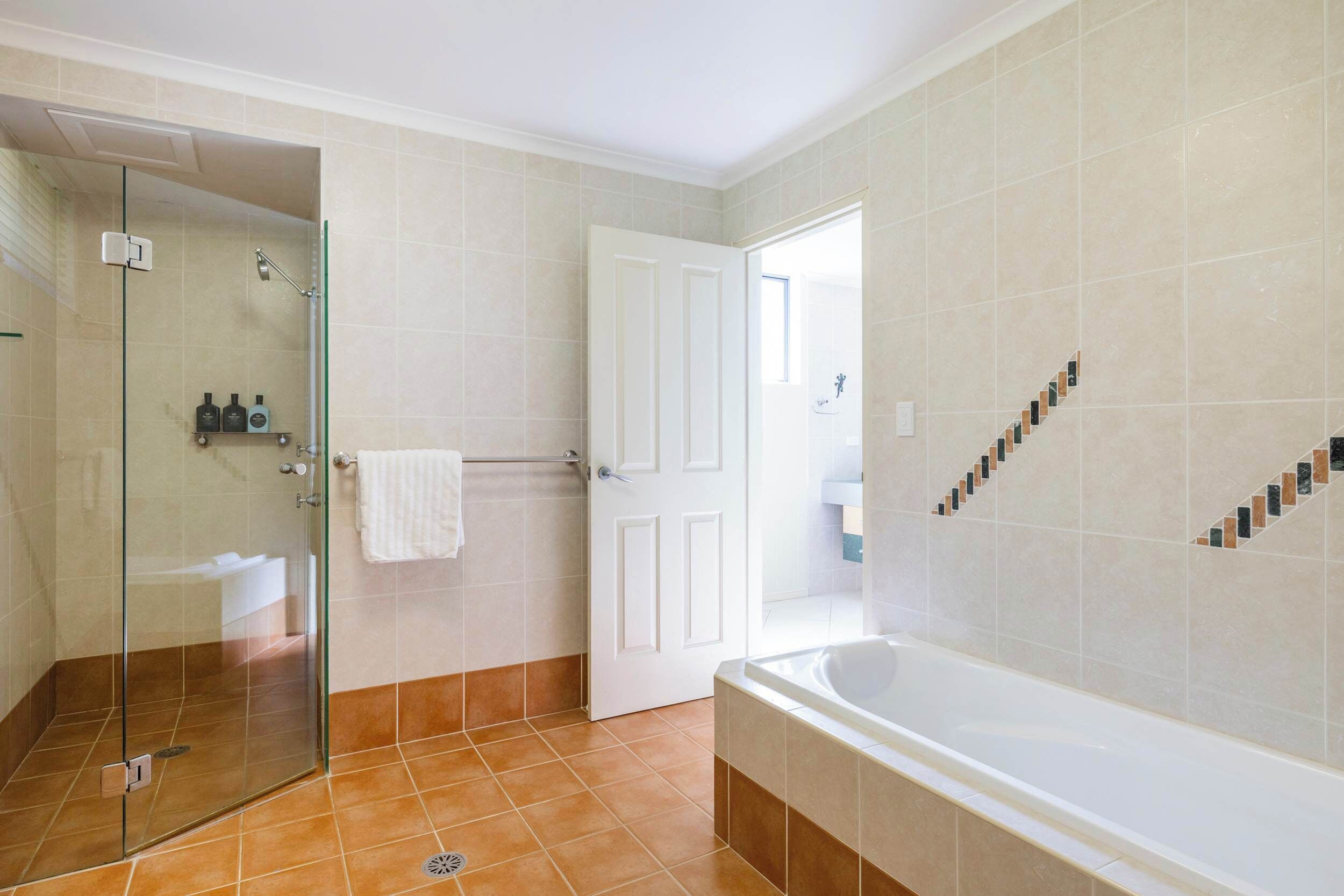 Ein Badezimmer mit Duschkabine aus Glas, einer Badewanne und einer weißen Tür.