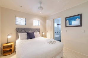 A bedroom with a bed, bedside lamps, a headboard, a framed picture, and a door leading to a bathroom. - Shadows on Convent - Oceanstays- Oceanfront- Pet friendly (Yamba)