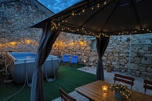 Eine Außenpatio mit Steinmauer, Whirlpool, Liegestühlen und einem Holztisch mit Kerze.