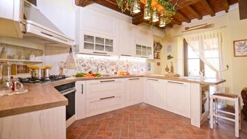Une cuisine avec des meubles blancs, un sol carrelé et un plafond en bois.