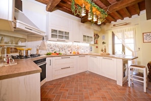 Una cucina con mobili bianchi, pavimento piastrellato e soffitto in legno.