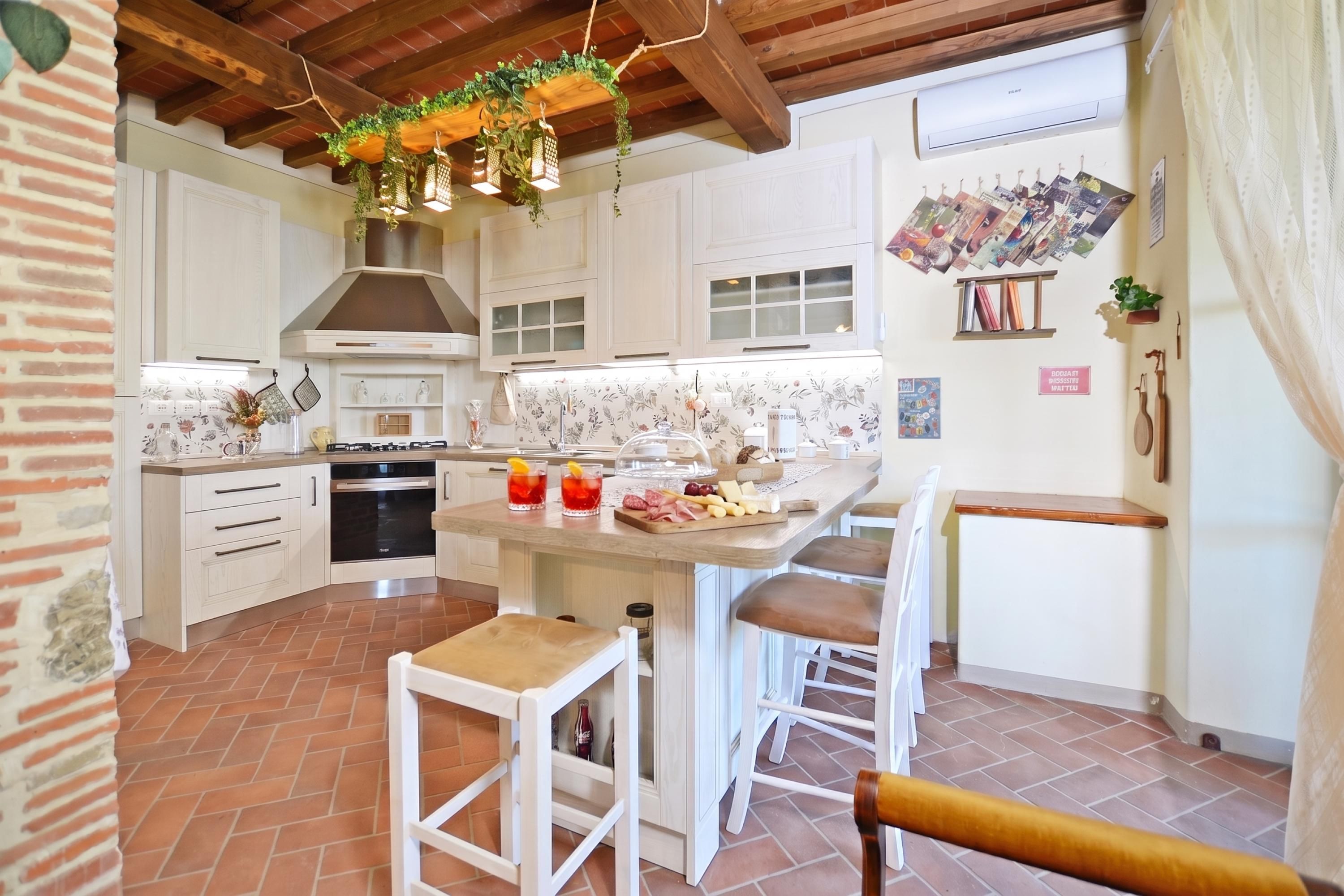 A kitchen with white cabinets, a central island with stools, hanging plants, and a tiled floor.
