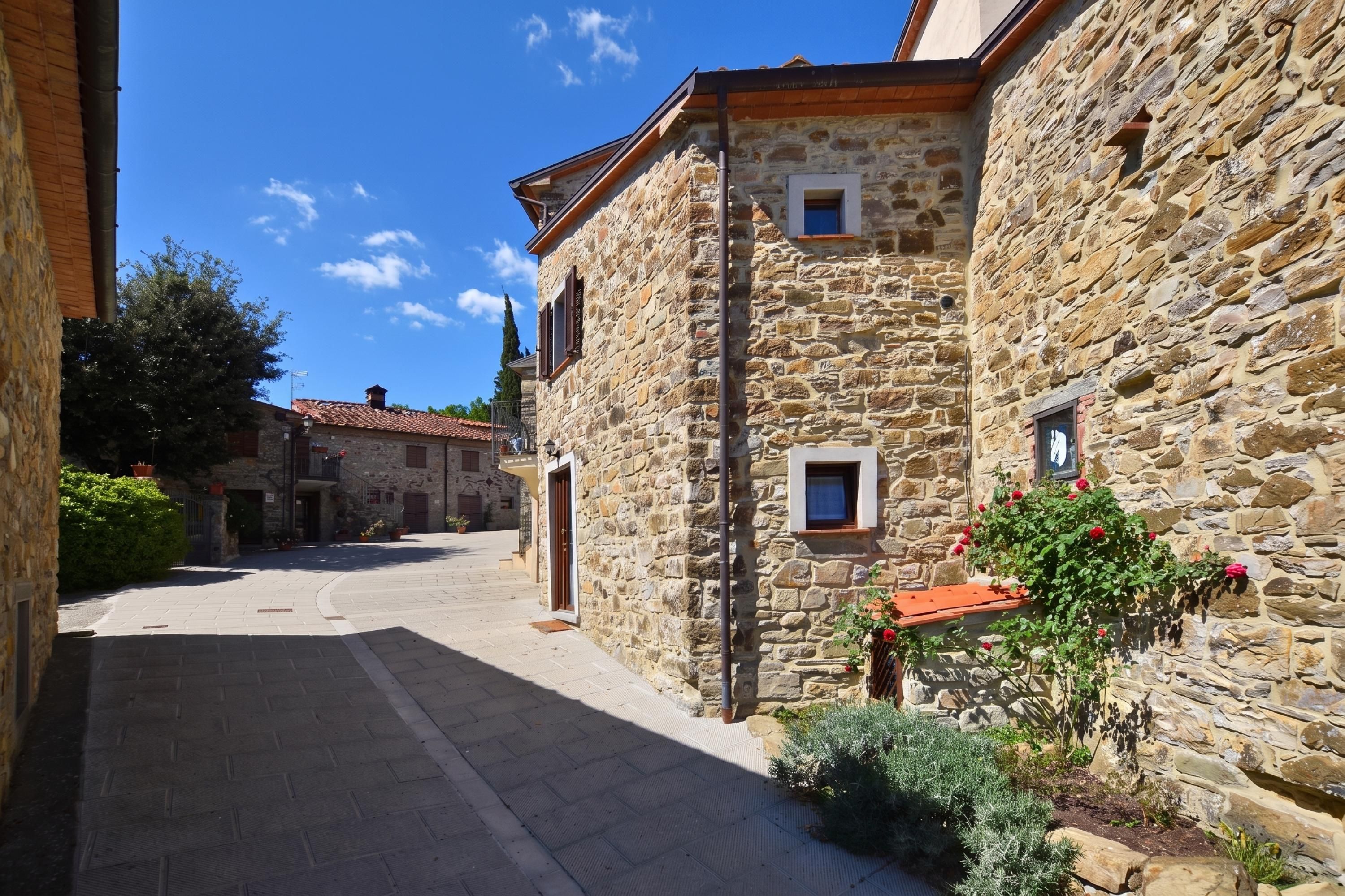 A stone building with a tiled roof, a narrow street, and a clear sky.