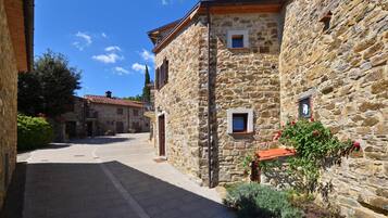 A stone building with a tiled roof, a narrow street, and a clear sky.