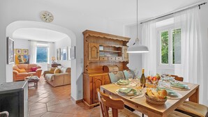 A dining area with a wooden table set for a meal, a kitchen with wooden cabinets, and a living room with a sofa and armchair. - Casa Berta Brissago 1 with Balcony for Four, Brissago, Switzerland (Brissago)