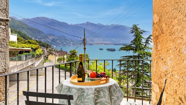 A balcony with a table set for a meal, overlooking a mountainous landscape and a lake. - Casa Berta Brissago 1 with Balcony for Four, Brissago, Switzerland (Brissago)