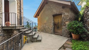A stone building with a wooden door, a balcony with a railing, and a potted plant. - Casa Berta Brissago 1 with Balcony for Four, Brissago, Switzerland (Brissago)