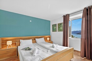 Ein Hotelzimmer mit einem großen Bett, zwei Nachttischen, einem fenster mit Vorhängen und Blick auf das Meer.