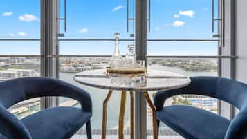 A room with a large window, two blue chairs, a round table with a glass top, and a decorative glass object on the table.