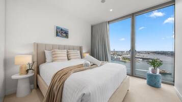 A modern hotel room with a large bed, a nightstand, a window with a city view, and a potted plant.