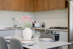 Eine moderne Küche mit Holdekor-Schränken, einer weißen Arbeitsplatte und einem Esstisch für vier Personen, dekoriert mit einem Blumenstrauß.