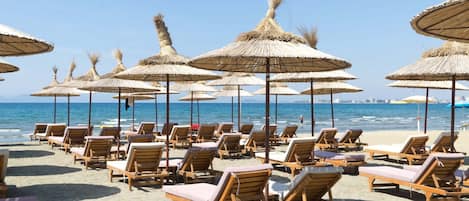 Una playa con filas de sillas de madera y sombrillas de paja.