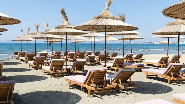 Una playa con filas de sillas de madera y sombrillas de paja.