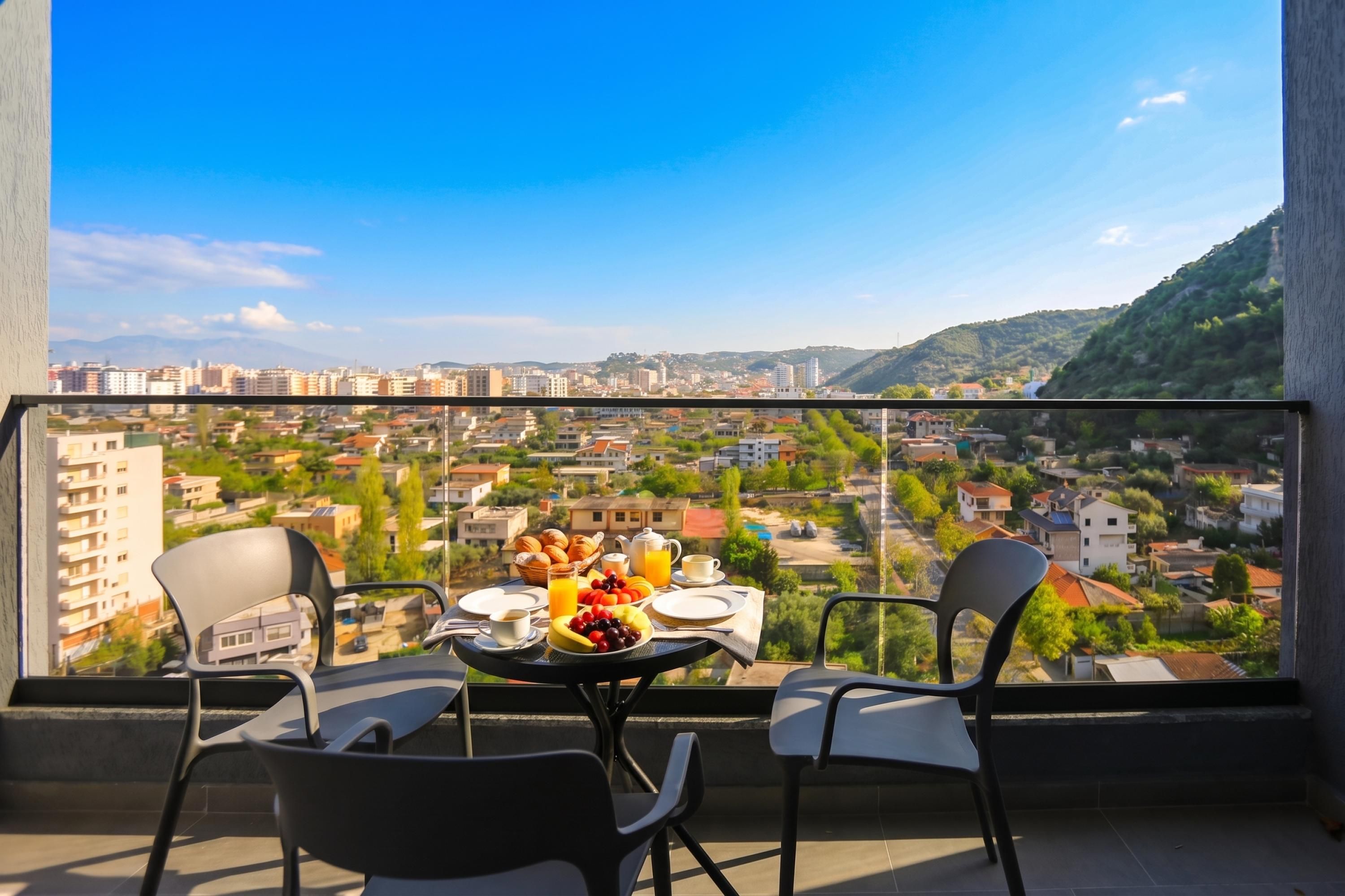 Een balkon met een ontbijttafel, met uitzicht op een stadsbeeld met gebouwen en heuvels.