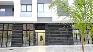 Un edificio moderno con ventanas amplias, una entrada negra y una palmera en primer plano.
