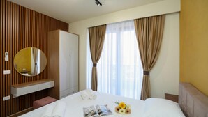 Habitación de hotel con cama, mesita de noche, espejo, armario y ventana con cortinas.