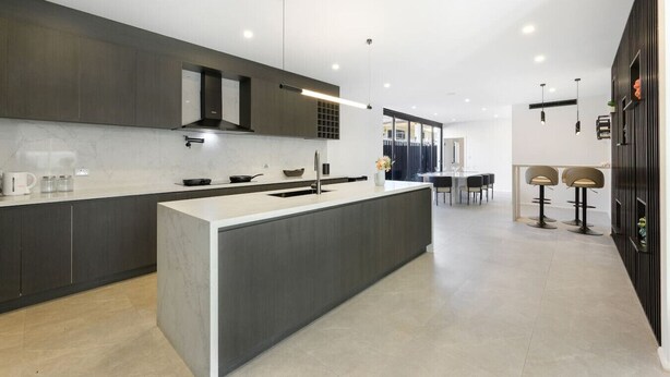 A modern kitchen with a central island, dark cabinetry, and a dining area with bar stools. - Spacious 5BR House for 14ppl/Family Gathering/Park (Kingsgrove)