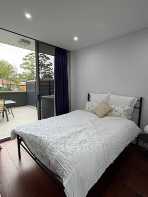 Ein Schlafzimmer mit Bett, einem Sessel, einem kleinen Tisch und Blick nach außen.
