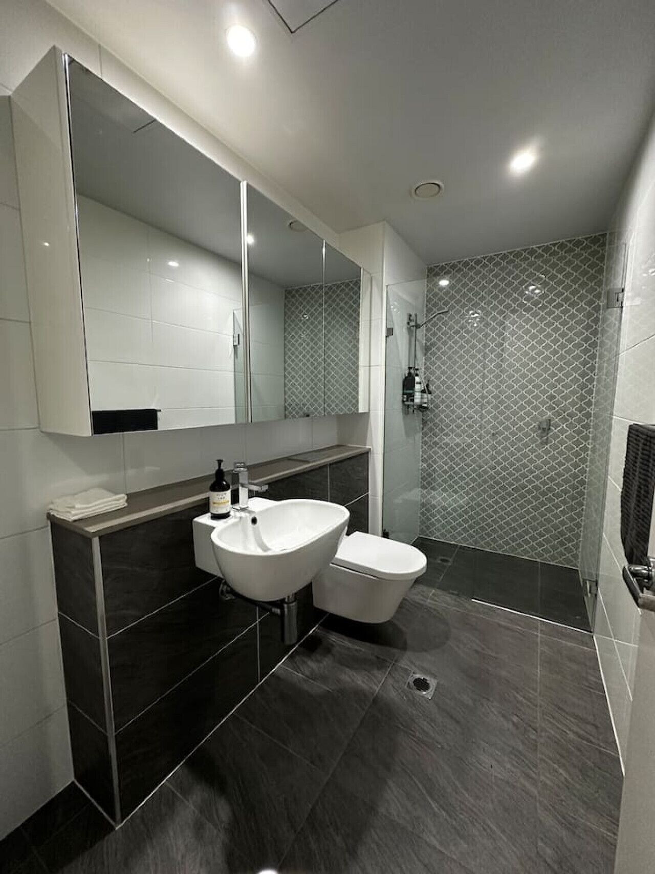 Een moderne badkamer met een grote spiegel, een wit wastafelmeubel, een toilet en een douchehoek.