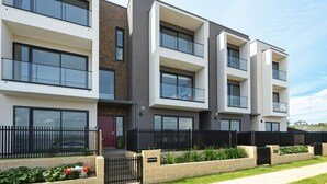 Ein modernes, mehrgeschossiges Wohngebäude mit großen Fenstern, einer Ziegel-Fassade und einem schwarzen Metallzaun.