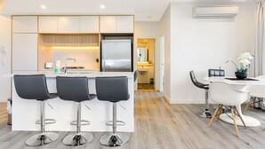 Een moderne keuken met een centraal eiland, drie barkrukken en een eethoek met een tafel en stoelen.