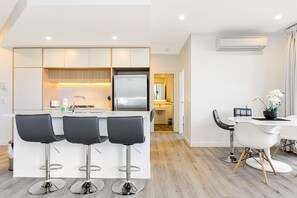 A modern kitchen with a central island, three bar stools, and a dining area with a table and chairs.