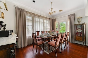 A dining room with a wooden table set for four, surrounded by chairs, a chandelier, and a vintage clock.