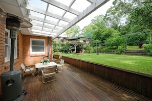A covered patio with a table and chairs, a brick wall, and a view of a backyard with a lawn and trees.
