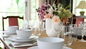 Une table à manger dressée avec de l’assiette blanche, des bols et des verres en cristal, et un vase de fleurs placé au centre.