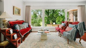 Une pièce avec un canapé rouge, un fauteuil rouge, une table basse en verre et une vue sur la verdure à l’extérieur.