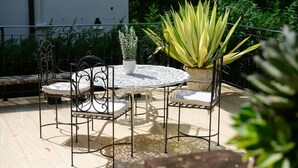 Une terrasse avec une table ronde et des chaises, entourée de plantes en pot.